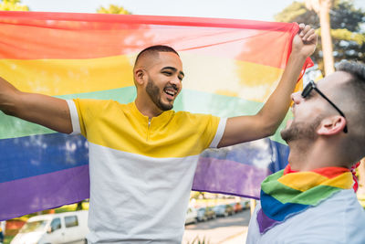 Gay couple with rainbow flag standing in city