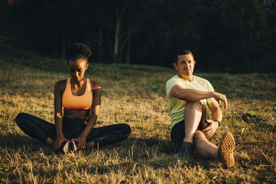 Sportsman and sportswoman doing relaxation exercise while sitting on grassy area