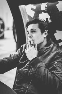 Young man smoking while sitting on sea at city street