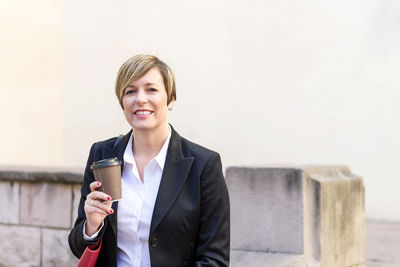 Portrait of young businesswoman standing against wall