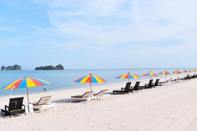 Lounge chairs with parasols arranged on beach against sky