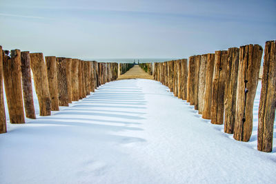 Wooden posts on snow covered land against sky