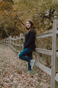 Portrait of smiling young woman standing by railing during autumn