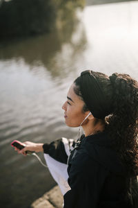 Female athlete with smart phone listening music while sitting by pond in public park