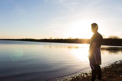 Rear view of woman standing by lake against sky