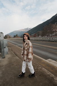 Portrait of smiling young woman standing on road against sky