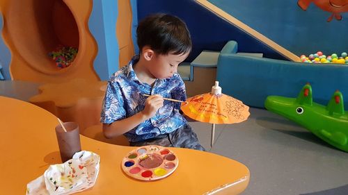 Boy painting small umbrella at table