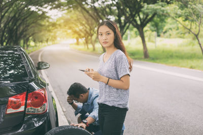 Worried couple by damaged car on road 