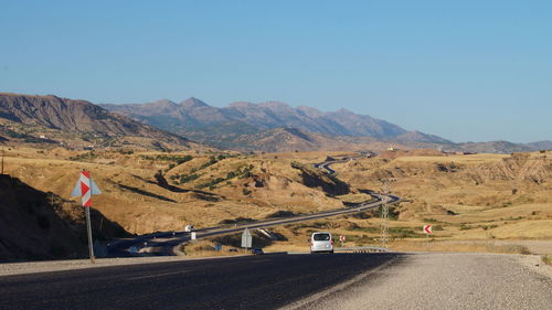 Country road leading towards mountains against blue sky