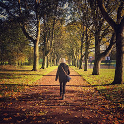 Rear view of woman walking on street amidst trees during autumn