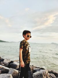 Portrait of young man standing at beach against sky during sunset