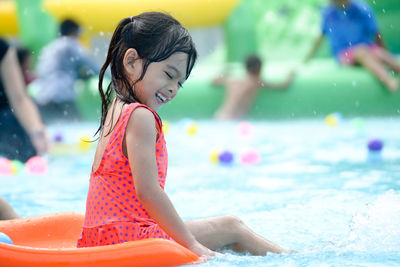 Side view of cheerful girl sitting on water slide in swimming pool