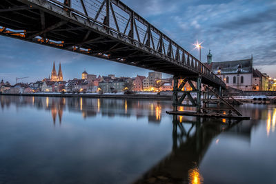 Illuminated bridge over river against sky in city at dusk