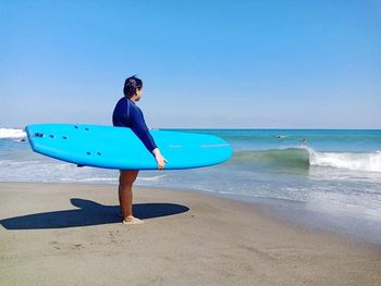 Man with surfboard on beach against blue sky