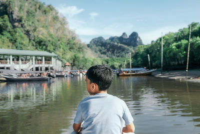 Rear view of boy by lake against sky