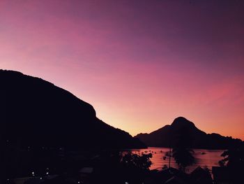 Silhouette mountains by sea against romantic sky at sunset