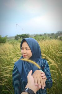 Cropped image of man holding woman hand amidst plants on field