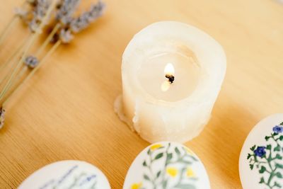 Top view of burning candle surrounded of chicken eggs painted with aquarelle placed on table with lavender flowers for easter