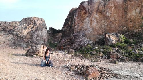 Woman crouching against rock formation