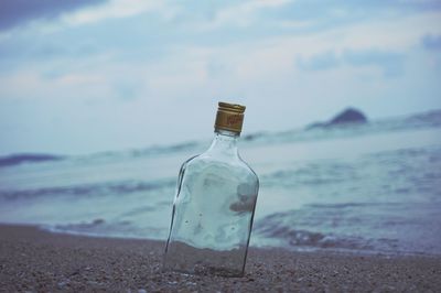 Close-up of wine bottle on beach against sky