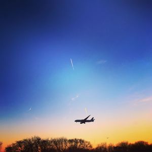 Low angle view of airplane flying in sky at sunset