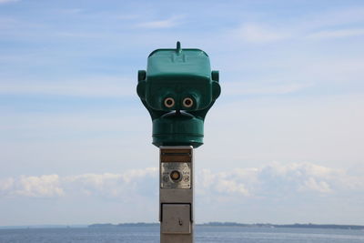 Close-up of coin-operated binoculars by sea against sky