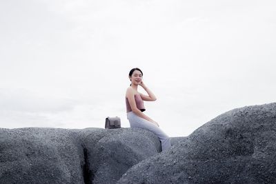 Woman sitting on rock against sky