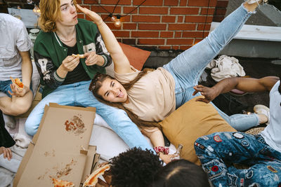 Portrait of happy woman sticking out tongue while lying by friends eating pizza on rooftop