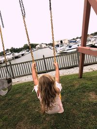 Rear view of girl swinging against clear sky at playground