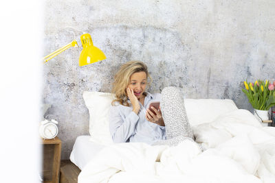 Mid adult woman using mobile phone while sitting on bed at home