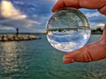 Close-up of hand holding crystal ball against sea