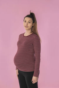 Portrait of young woman standing against pink background