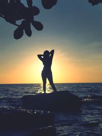 Silhouette woman standing on rock in sea against sky during sunset