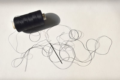High angle view of black thread with needle on white background
