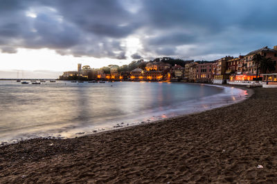 View of city at waterfront against cloudy sky