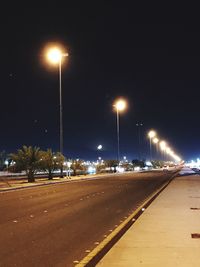 Empty road along illuminated street lights at night