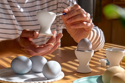 Woman preparing colored easter eggs and painting eggcup for easter holiday celebration.