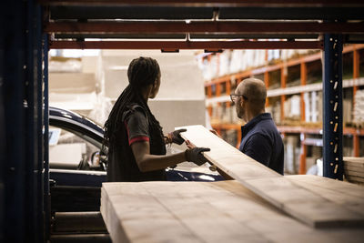 Female sales staff holding plank with male customer at hardware store