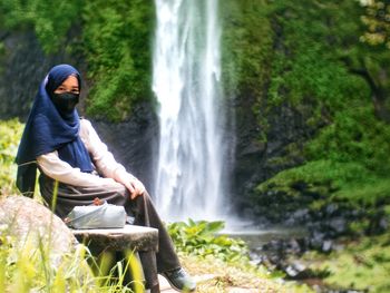 Rear view of female sitting against waterfall