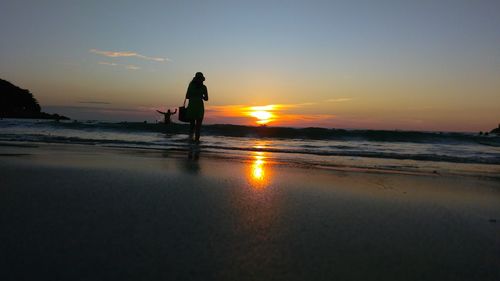 Low angle view of silhouette woman standing at kata beach against sky during sunset