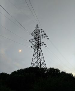 Low angle view of silhouette electricity pylon on field against sky at sunset