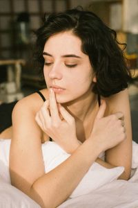 Young woman looking away while sitting on bed at home