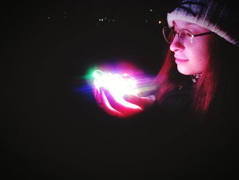 Close-up of woman holding illuminated lighting equipment against black background