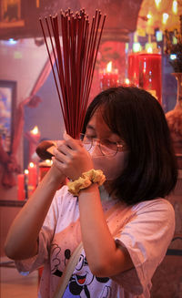 Front view of woman holding incense and praying in temple