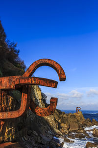 Rusty metallic structure by sea against clear blue sky