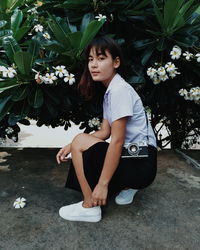 Side view portrait of young woman crouching by plants