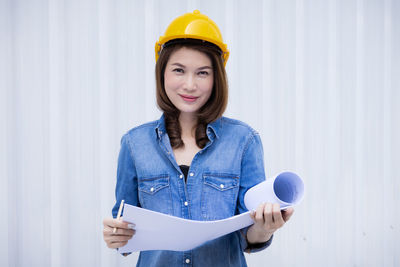 Portrait of smiling young woman wearing hat standing against blue wall