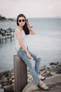 Young woman wearing sunglasses on rock at sea shore