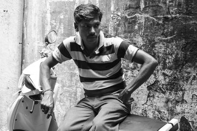 Portrait of young man sitting against wall