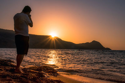 Silhouette of man standing on beach at sunset